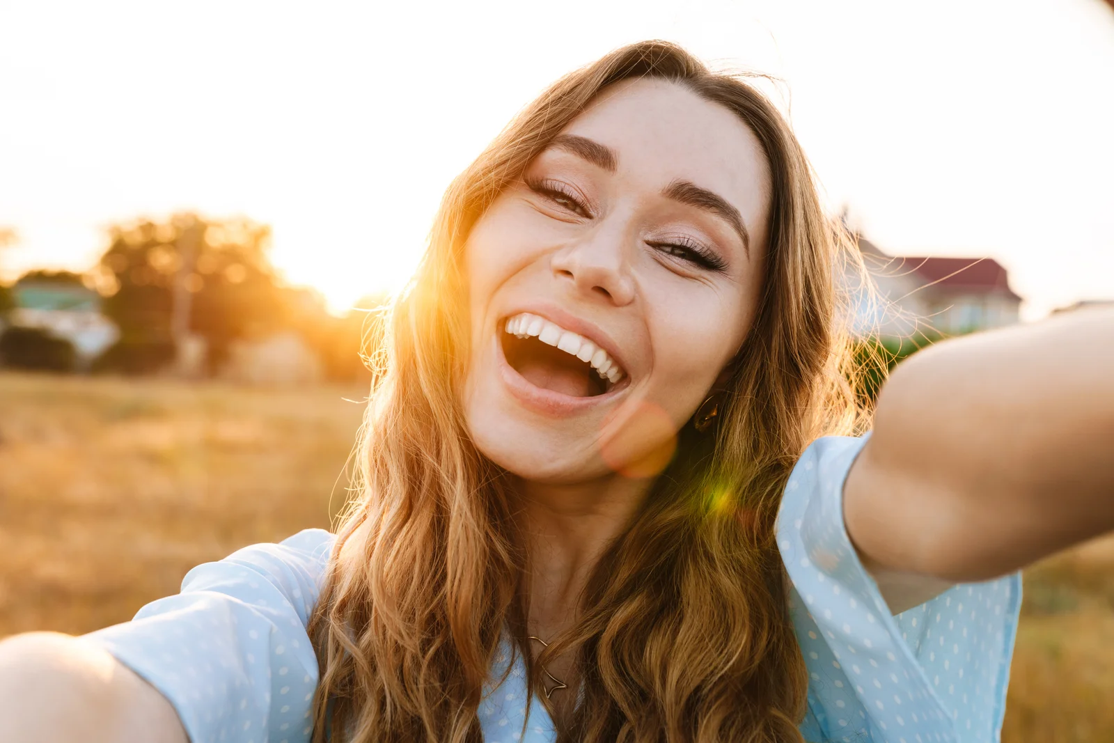 A smiling woman taking a selfie outdoors at sunset