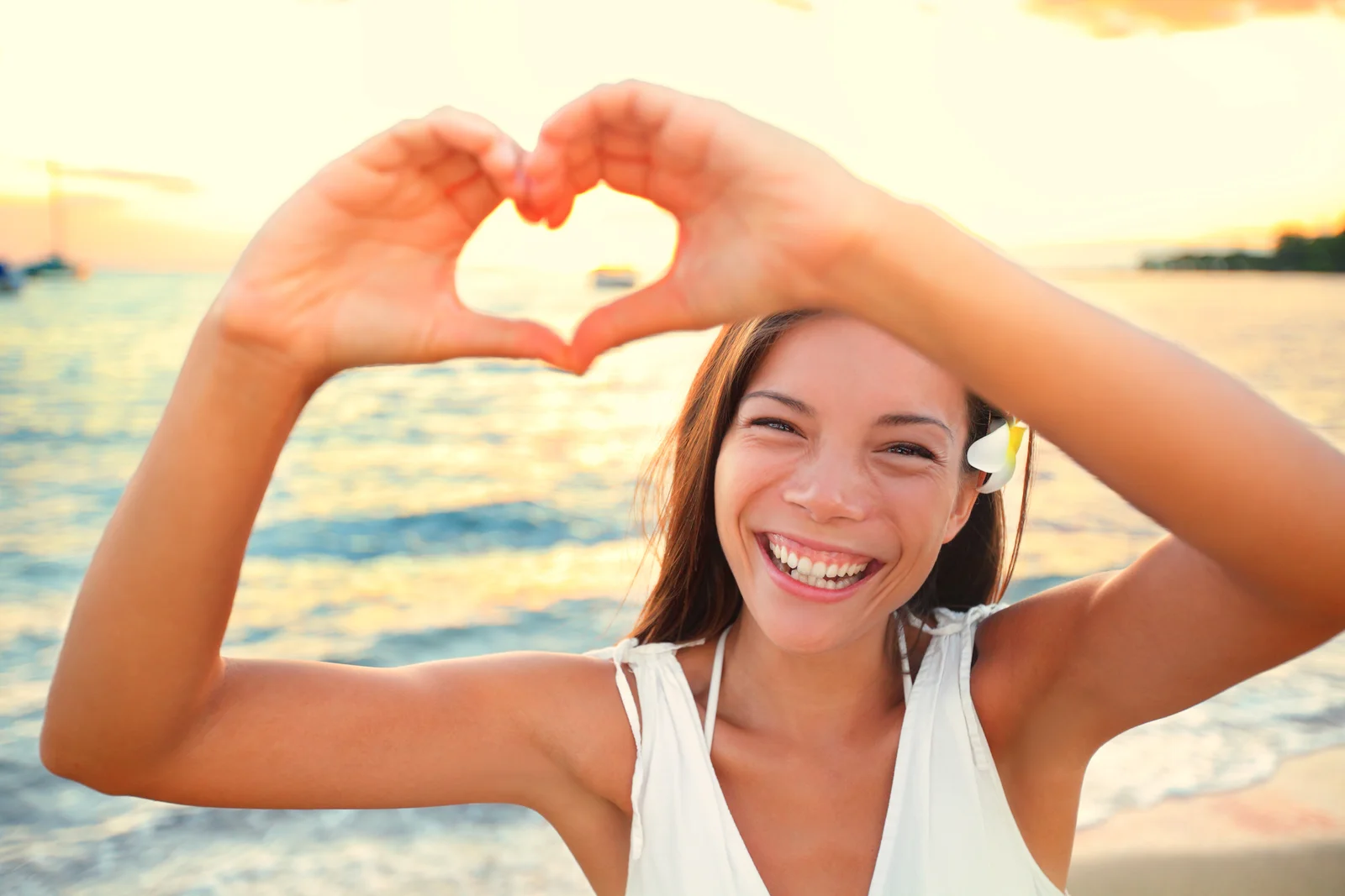 A smiling woman making a heart with her hands at the beach